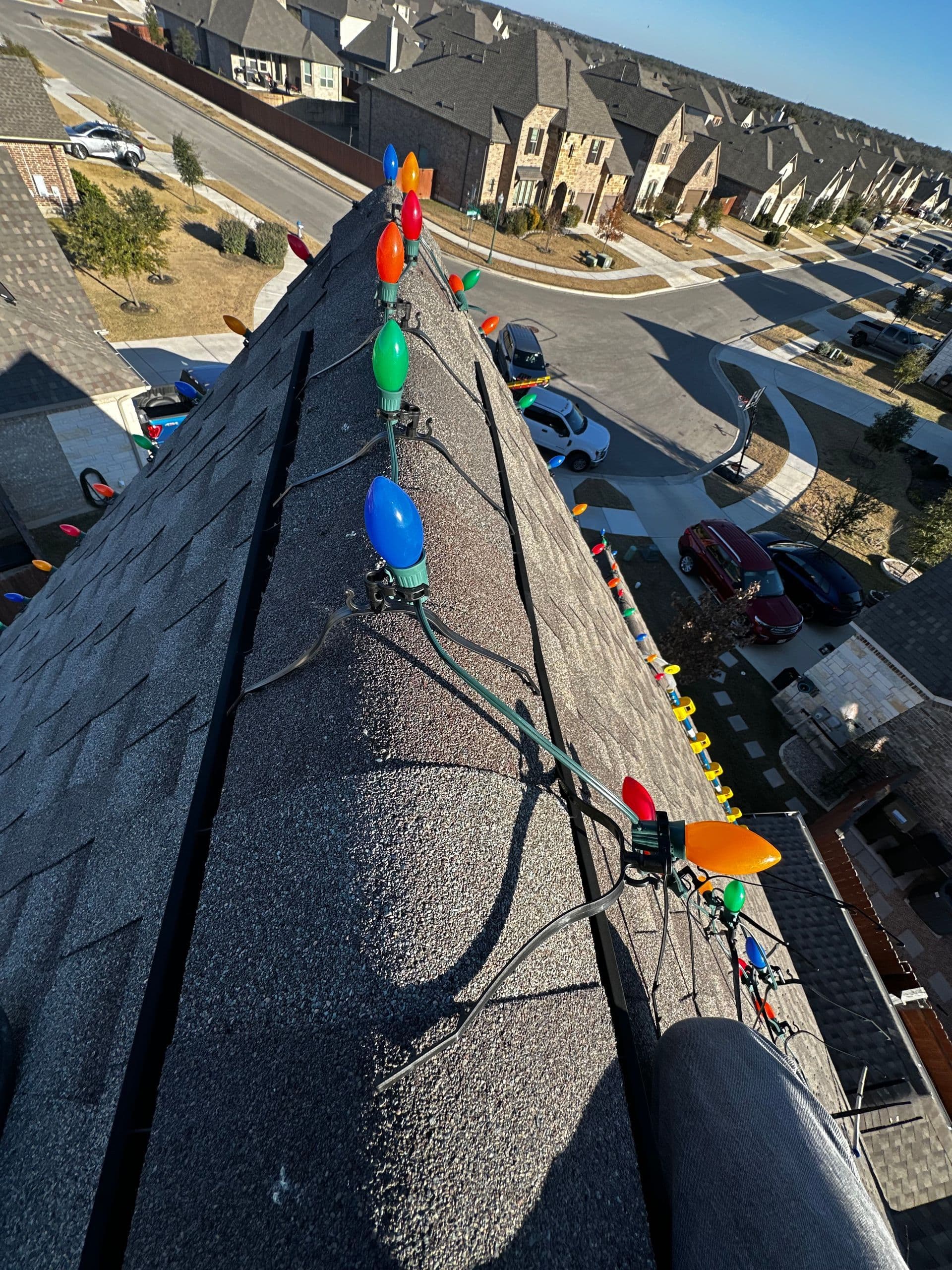 Multicolored Christmas bulbs clipped along a roof ridge above a Texas neighborhood.