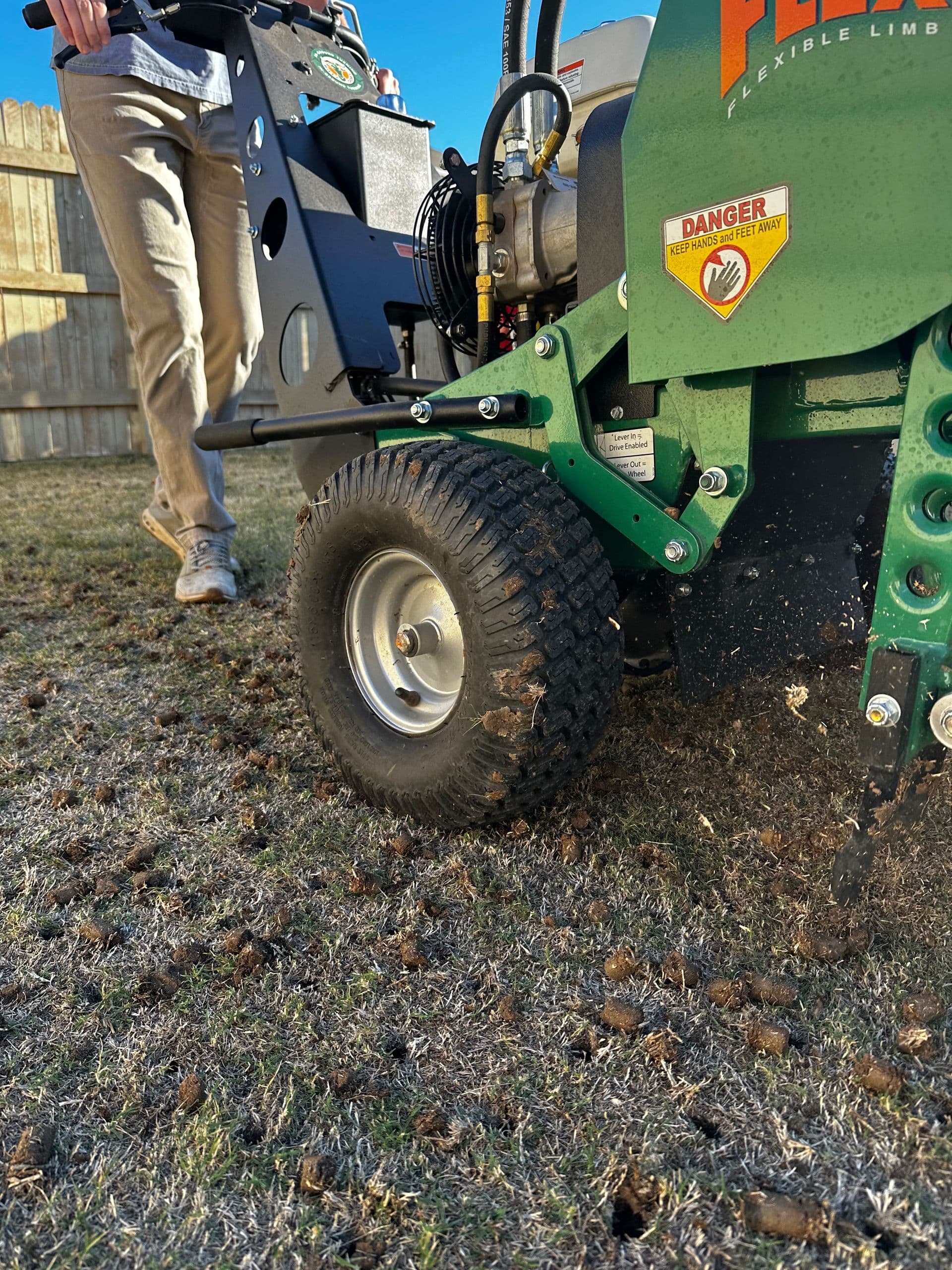 Technician walking a green core aerator across a lawn, leaving soil plugs behind.