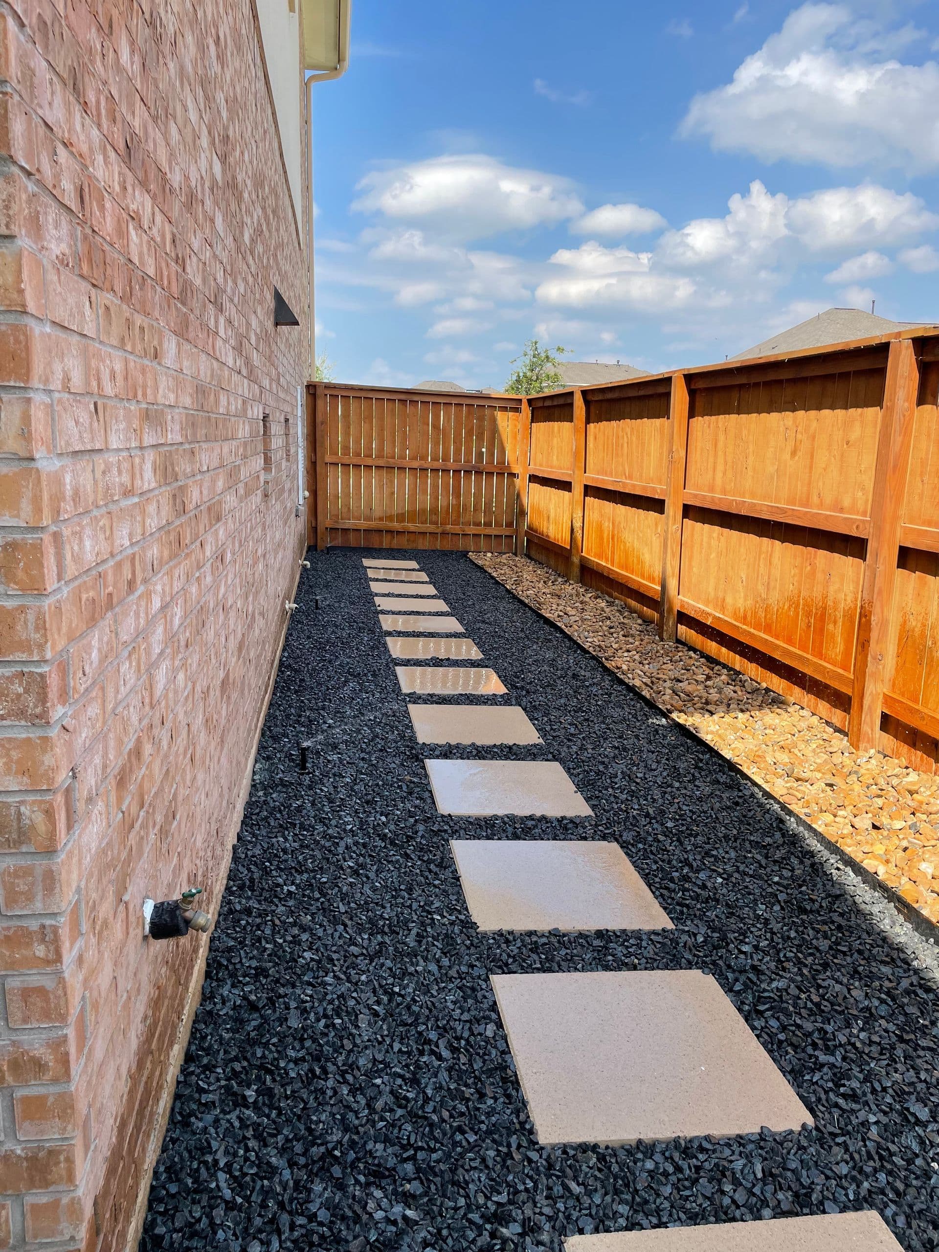 Concrete paver stepping stones set in black gravel along the side of a brick home.