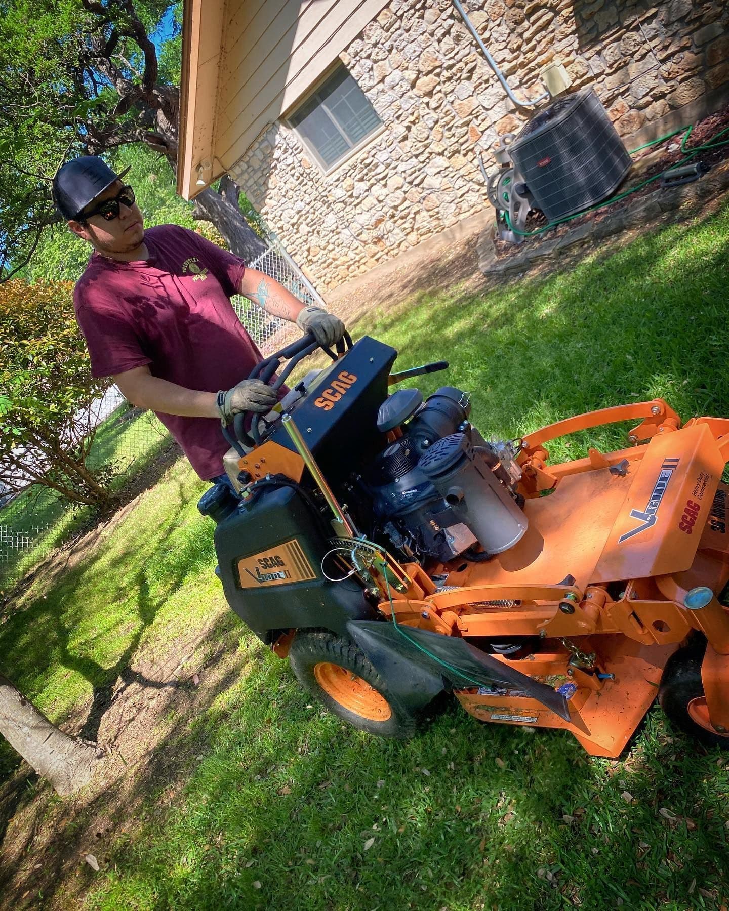 Man operating orange riding lawn mower on green grass by stone house