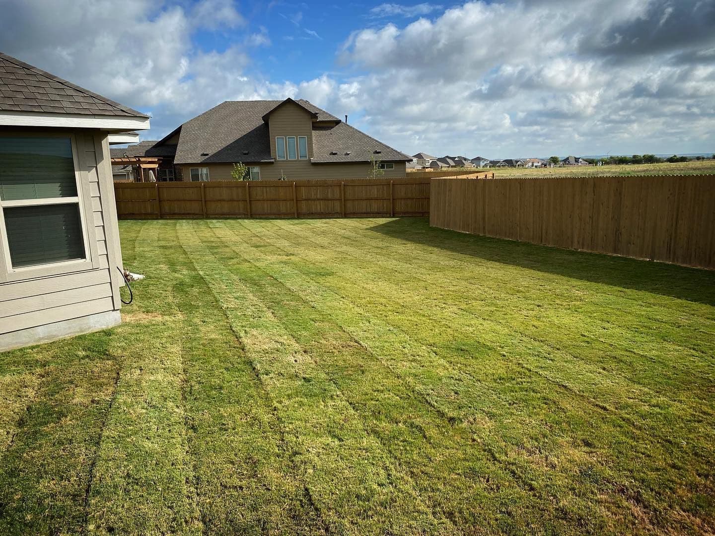 Large fenced backyard with fresh mowing stripes across healthy green grass.