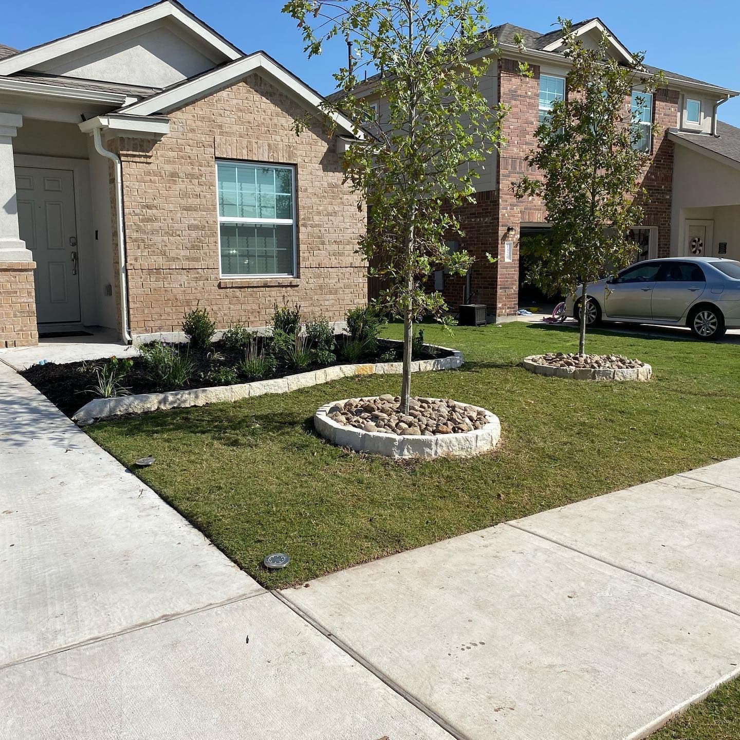 Front yard of a brick home with new planting beds, staked young trees and fresh sod.