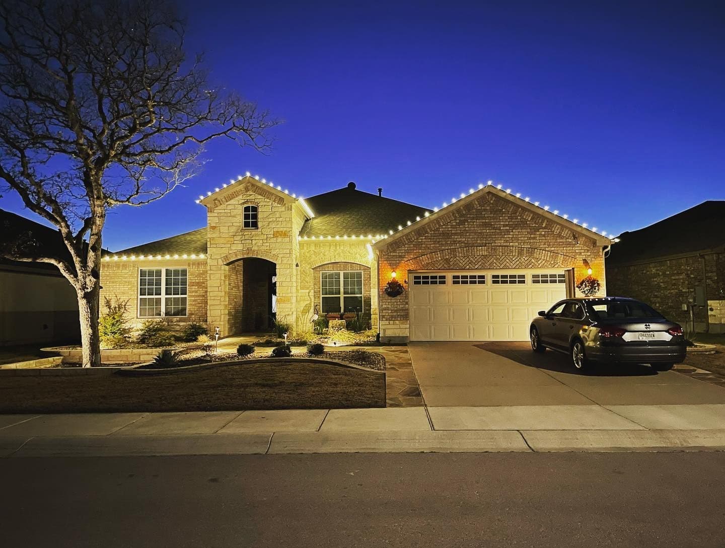 Stone Texas home outlined in warm white Christmas lights at dusk.
