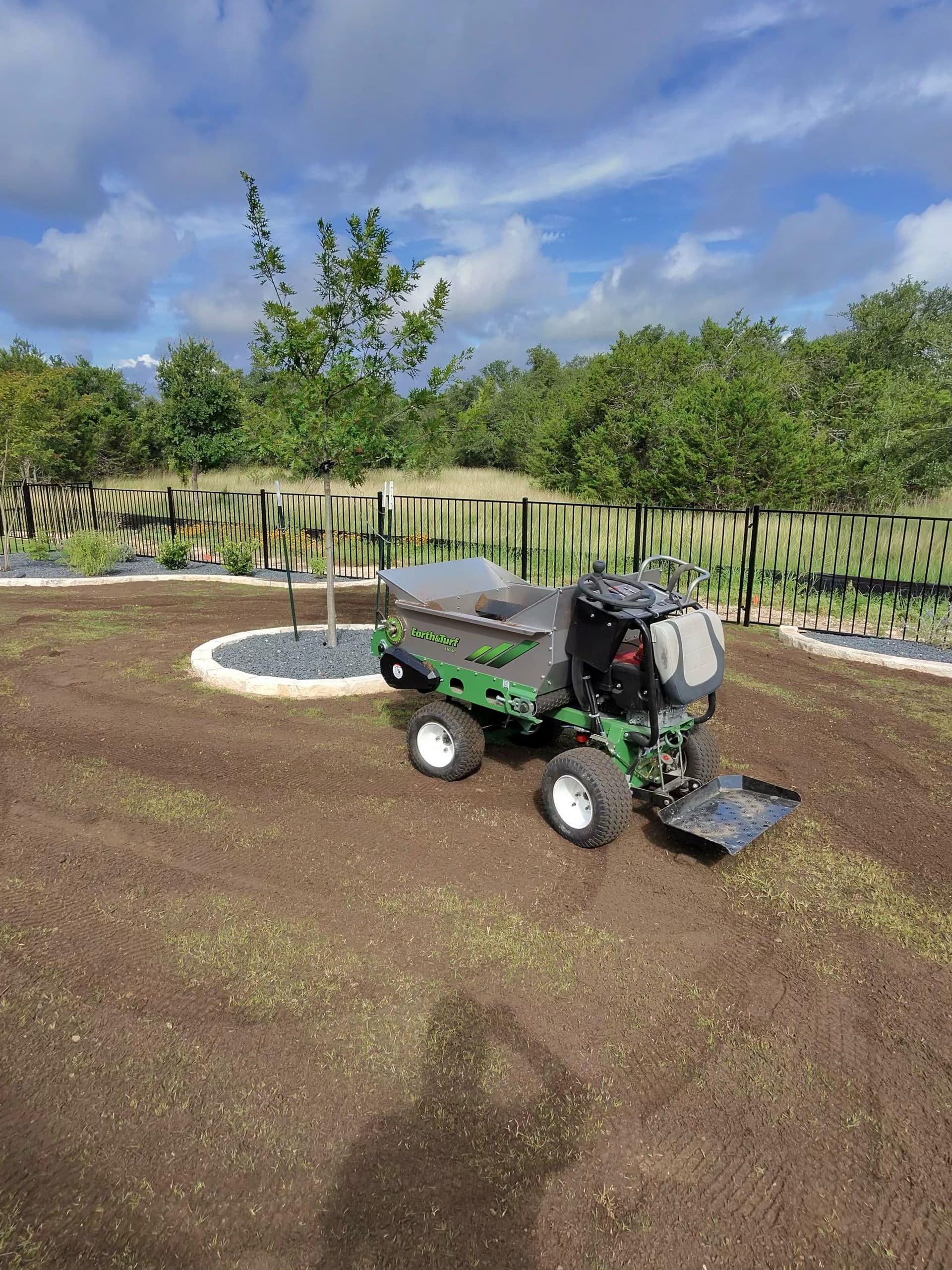 Green tracked dumper parked on freshly graded soil in a fenced yard, ready for sod installation.
